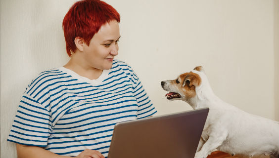 Kvinde med bærbar computer på skødet smiler til sin hund